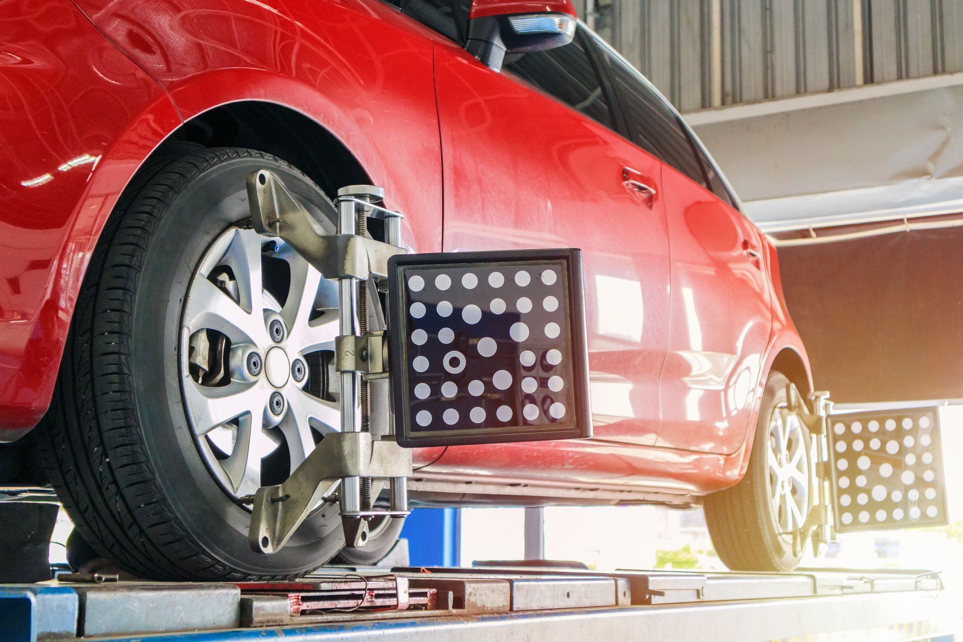 Red car on a lift, wheel alignment tools attached. | Autovantage Service Center
